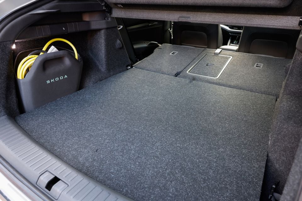 Boot space of a Skoda Enyaq with rear seats folded flat, showing a charging cable bag with Skoda branding stored to the side