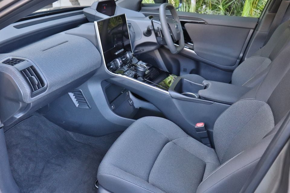 Interior of a 2026 Subaru Solterra showing the front seats, centre console, large touchscreen infotainment display, and steering wheel, viewed from the passenger side door