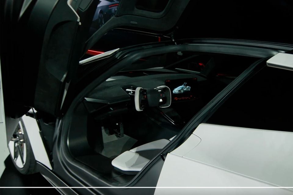 The cabin of the 2026 Tesla Roadster seen through its open upward-swinging door, showing a yoke-style steering wheel, digital screen and white seat
