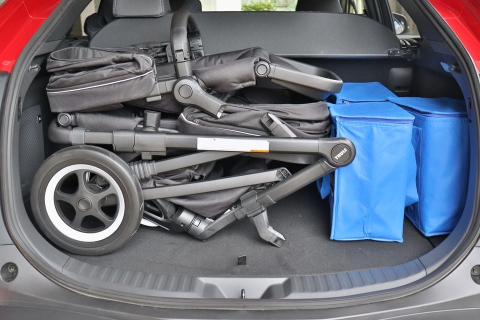 A folded Thule pram and blue bags loaded in the boot of a red 2026 Toyota bZ4X