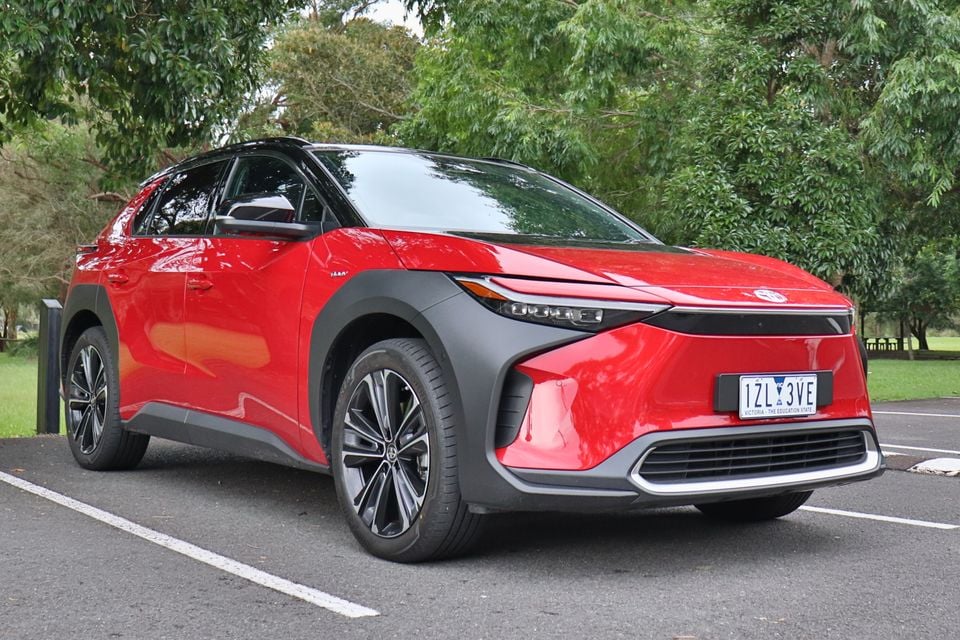 A red 2026 Toyota bZ4X SUV seen from the front-left side, parked in a car park with trees in the background