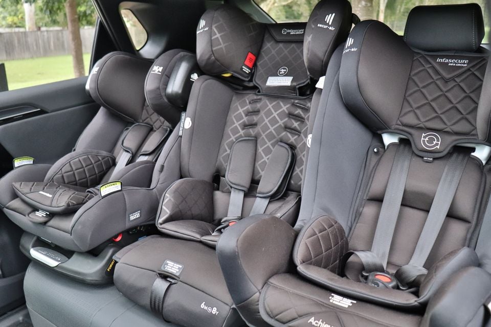 Three child car seats fitted side by side across the rear seat of a vehicle, including Infasecure models with harness straps