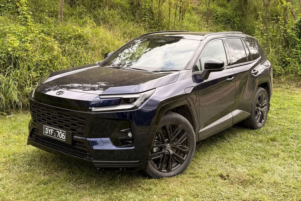 A dark blue 2026 Toyota RAV4 SUV with black alloy wheels parked on grass, seen from the front left