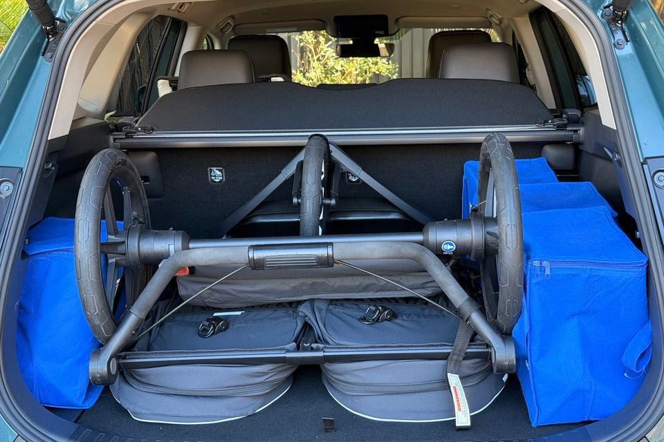 The boot of a 2026 Toyota RAV4 loaded with a folded twin pram and blue shopping bags, seen through the open tailgate