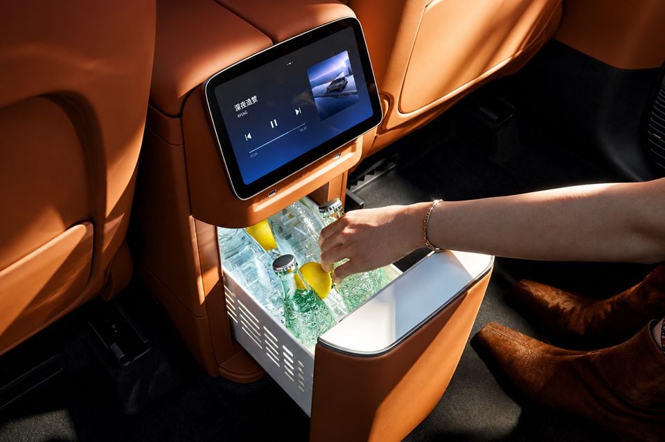 Interior of the 2026 Xpeng G9L showing a rear-seat fridge compartment with drinks and lemons, alongside a rear entertainment screen mounted on the front seatback