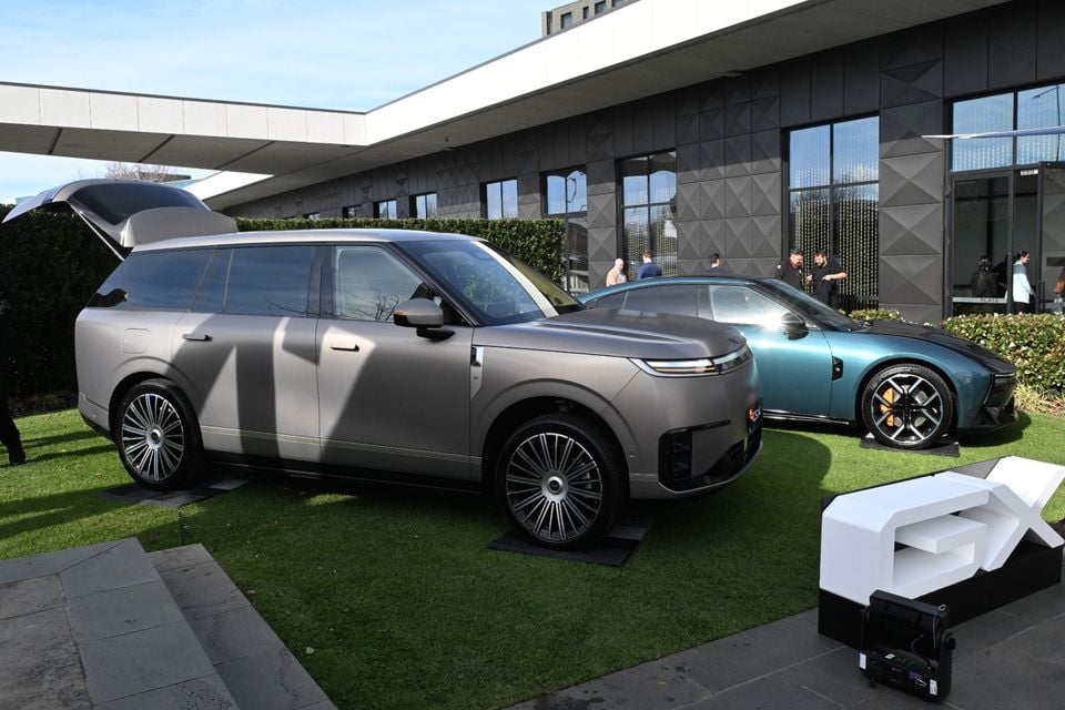 A grey 2026 Xpeng GX SUV on display at an outdoor event, with a green sports car visible behind it