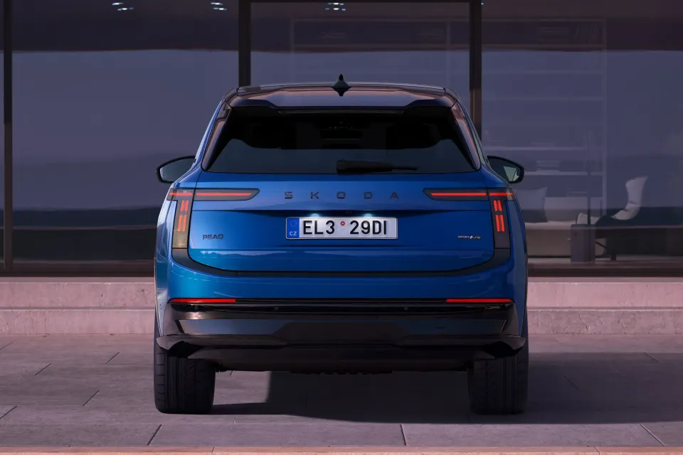 Rear view of a blue Skoda Peaq SUV SportLine variant parked outside a modern building at dusk