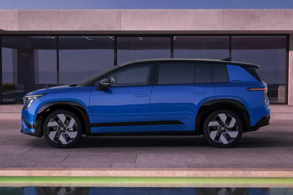A blue 2026 Skoda Peaq electric SUV seen from the side, parked outside a modern building at dusk.