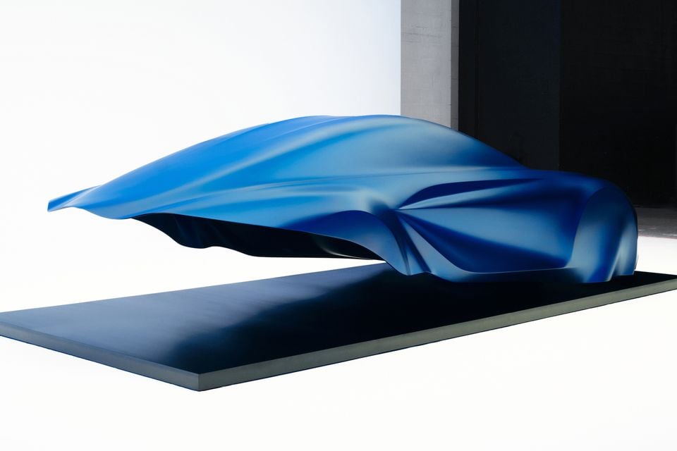 A car-shaped sculpture draped in a blue cloth, previewing the silhouette of an upcoming vehicle