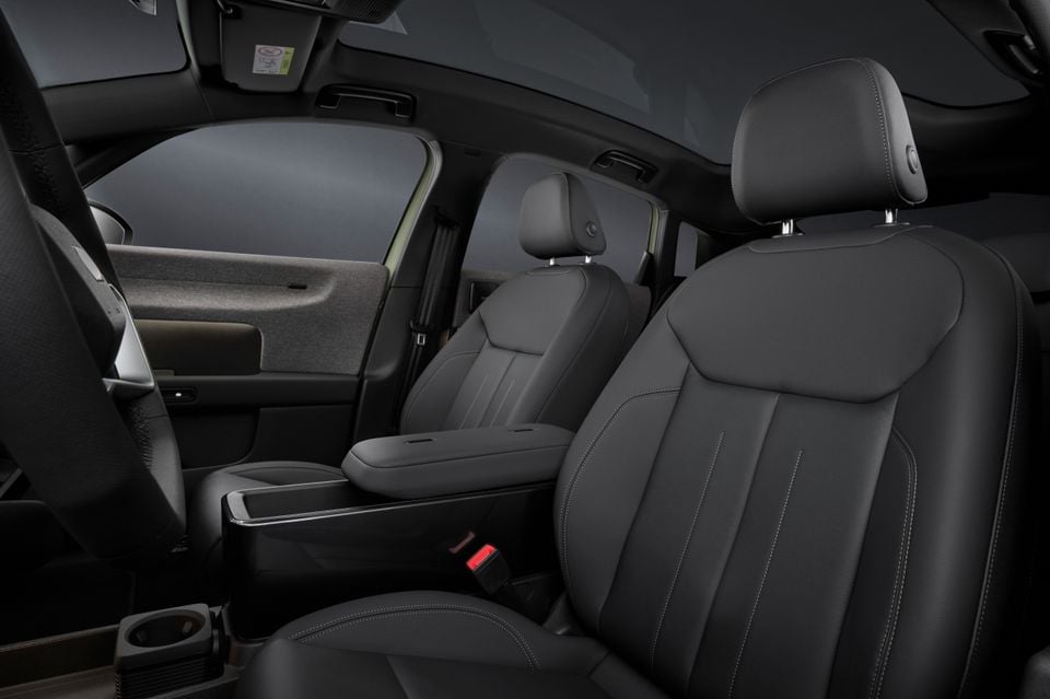 Interior view of a 2027 Audi A2 e-tron showing dark leather front and rear seats with white contrast stitching, centre armrest, and cup holder
