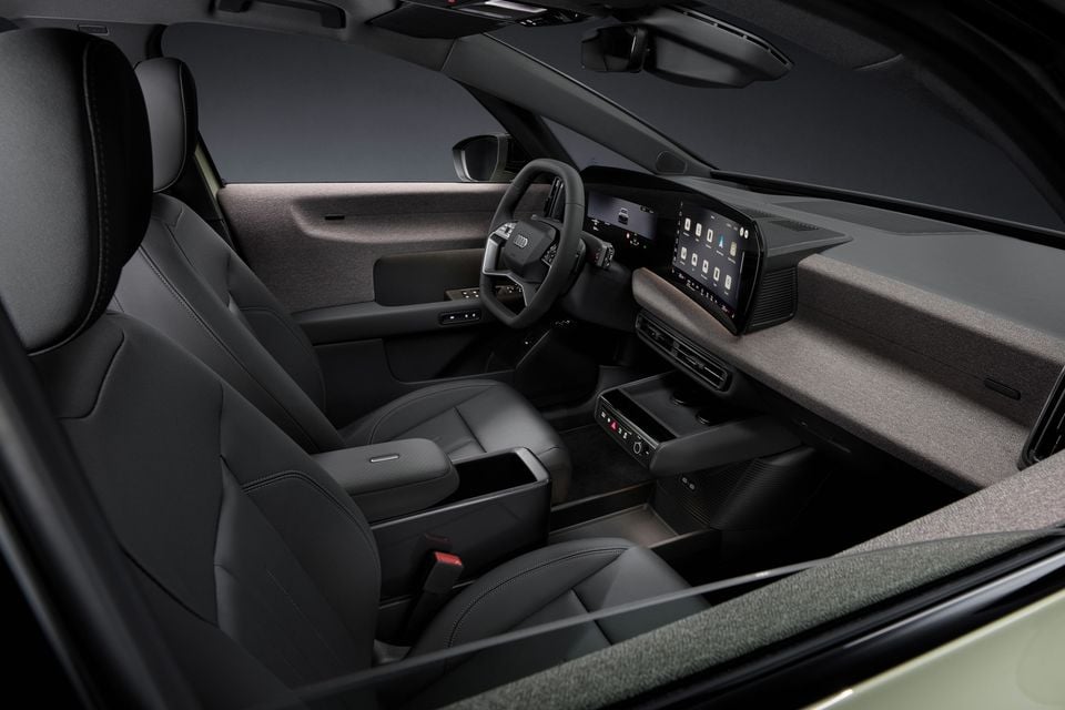 Interior of the 2027 Audi A2 e-tron showing the dashboard, steering wheel, wide infotainment touchscreen, front seats, and centre console with dark upholstery and textile trim accents