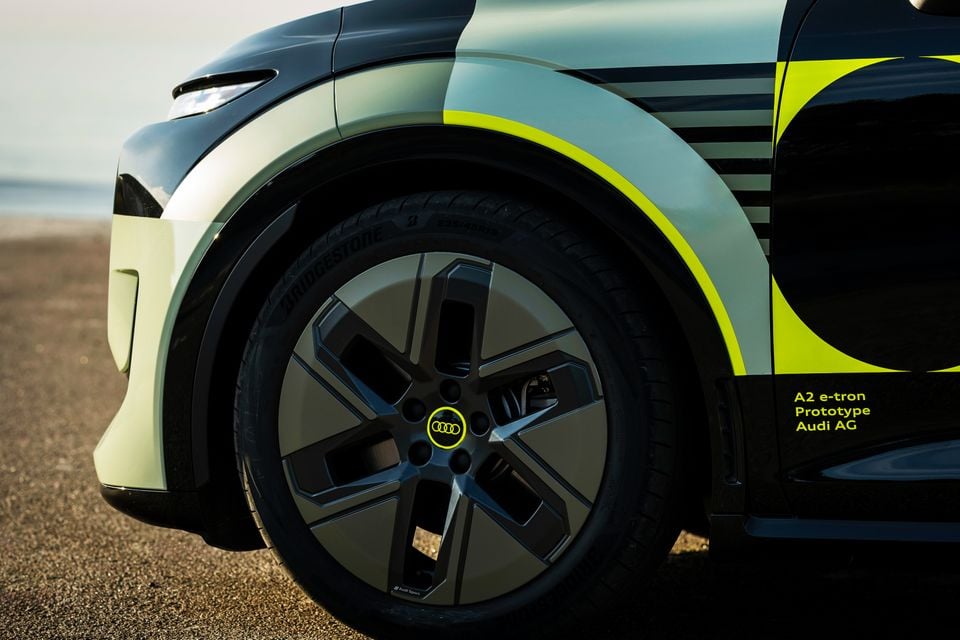 Close-up of the front wheel and fender of the Audi A2 e-tron Prototype, featuring a dark multi-spoke alloy wheel with a neon yellow Audi logo and Bridgestone tyre, set against a striking black and lime green wrap.