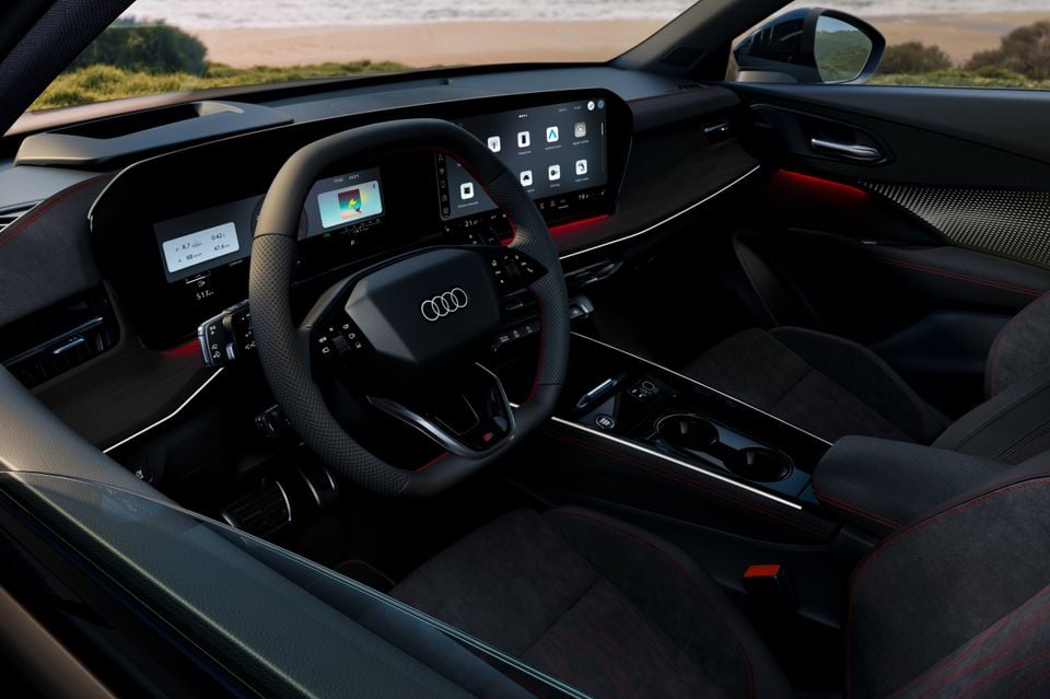 Audi Q3 interior showing the flat-bottomed steering wheel, digital instrument cluster, large central touchscreen displaying Apple CarPlay, and dark upholstery with red contrast stitching