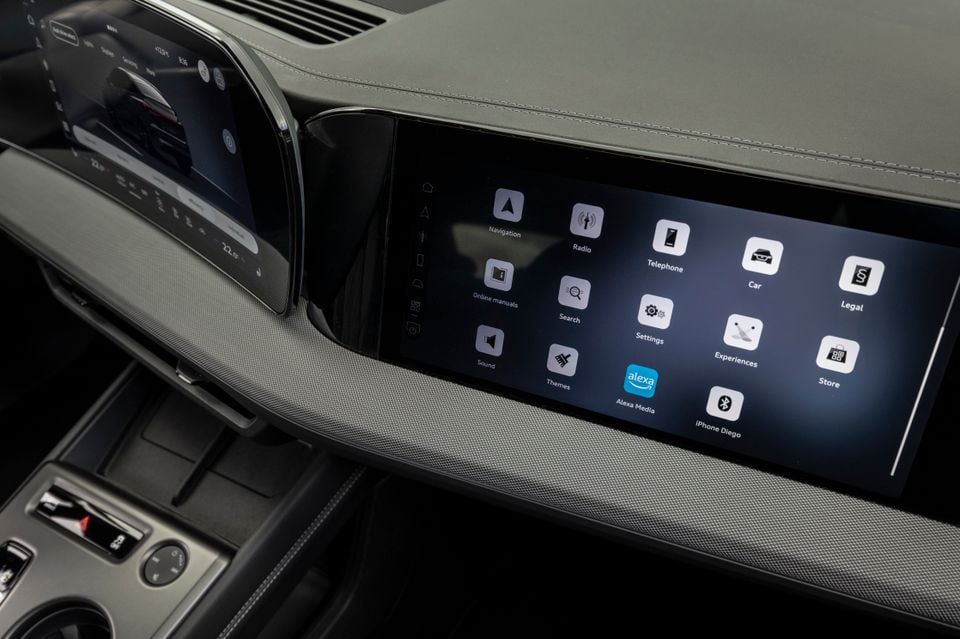 The central infotainment touchscreen of a 2027 Audi Q4 e-tron showing the main app menu, including Navigation, Radio, Alexa Media and Settings, alongside a secondary curved display