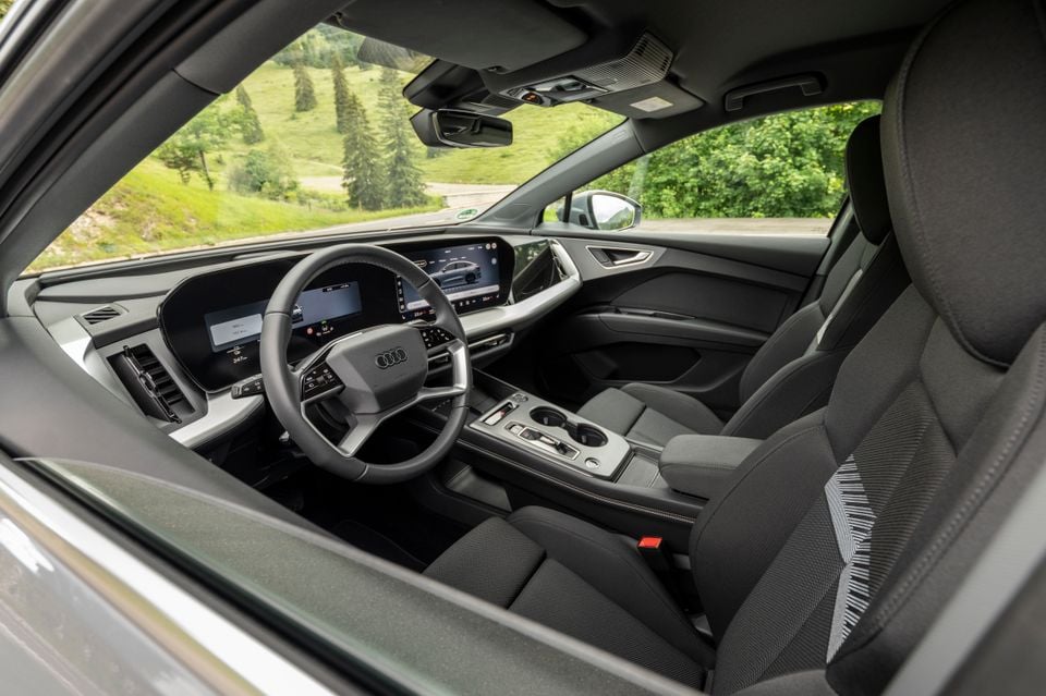 Interior of a 2027 Audi Q4 e-tron showing the dashboard, digital instrument cluster, infotainment screen, steering wheel, centre console and front seats, viewed through the open passenger door