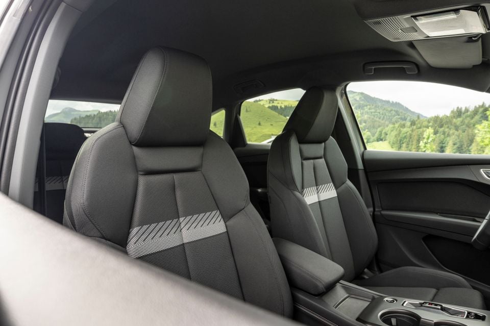 Interior view of a 2027 Audi Q4 e-tron showing front seats with dark fabric upholstery and geometric patterned inserts, with a scenic mountain backdrop visible through the windows