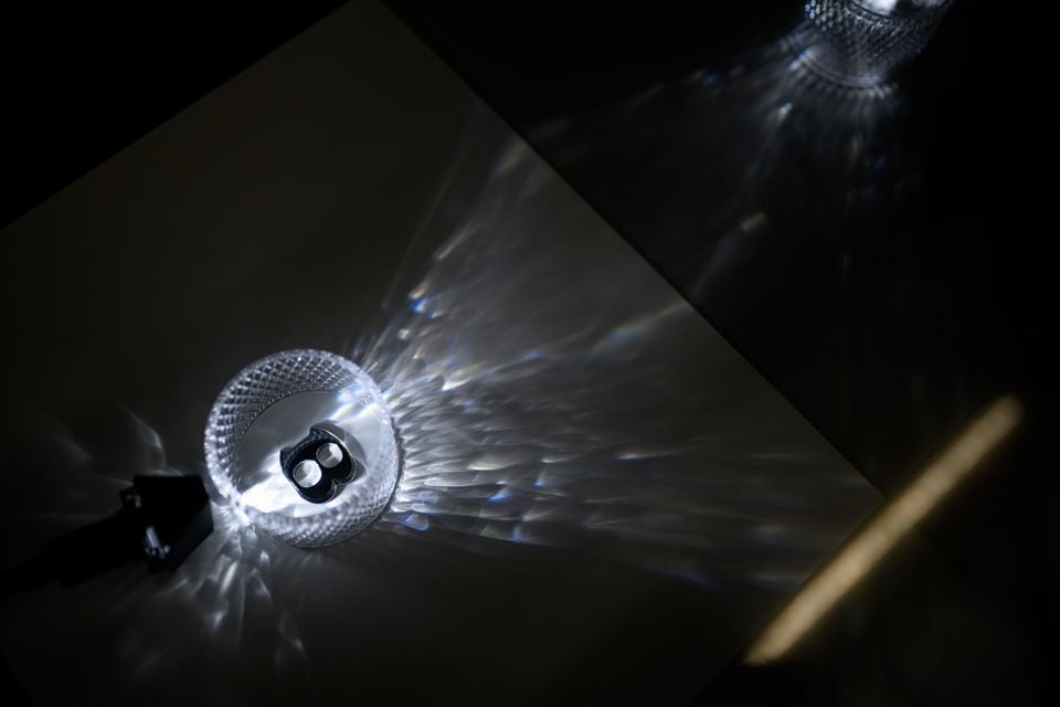 Um close de uma luz interna de cristal da Bentley projetando padrões de luz intrincados em uma superfície escura, com o logotipo 'B' da Bentley visível no centro