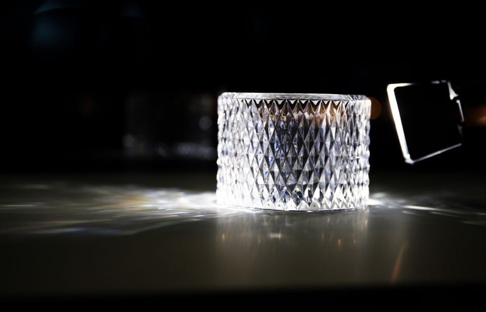 A crystal-cut glass vessel with diamond-pattern facets catching light on a dark reflective surface, with a Bentley gear selector visible in the background
