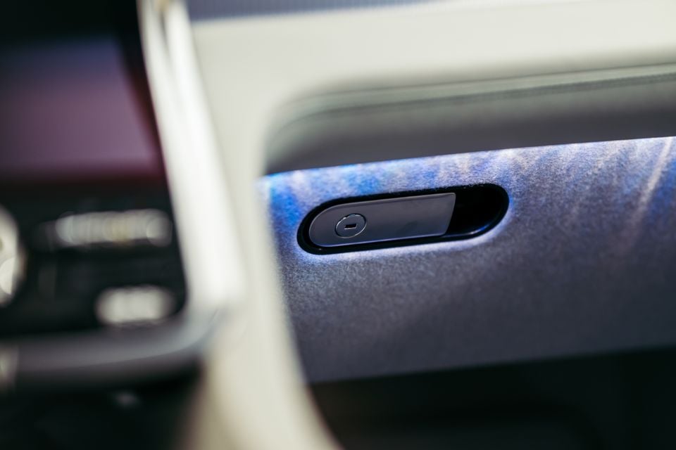 Close de um recesso de maçaneta de porta com um botão no painel interno de um carro com acabamento em camurça, provavelmente de um Bentley Torcal