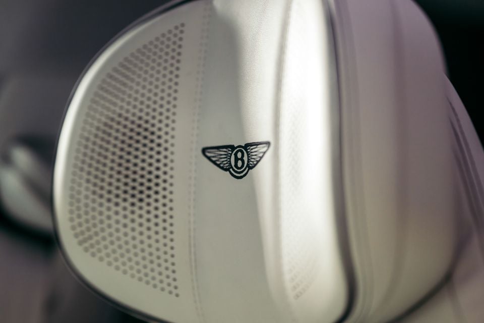 Close-up of a Bentley logo embroidered on a leather seat headrest with a perforated pattern