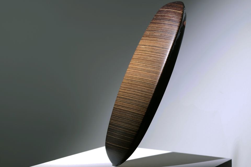 A teaser image of an abstract sculptural design element for the upcoming Bentley Torcal, featuring a dark elliptical disc with fine linear texture on a white plinth