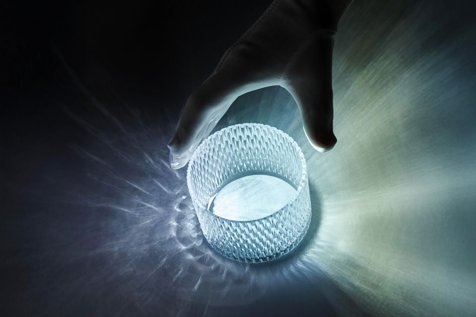 A hand holding a glowing textured crystal glass object that emits radiating light beams, shown as a teaser image for the 2027 Bentley Torcal