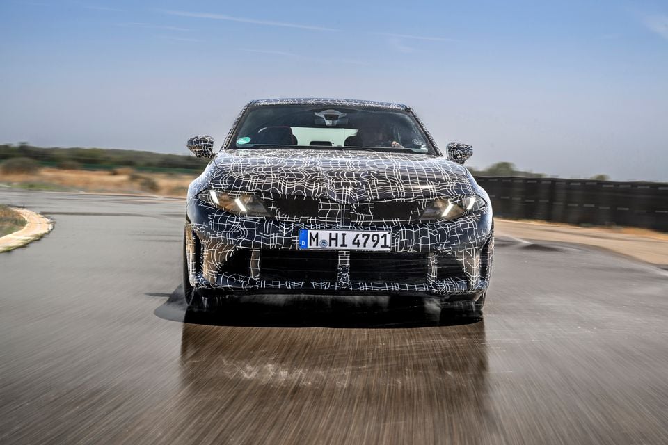 A camouflaged 2027 BMW 3 Series prototype seen from the front while being driven on a test track