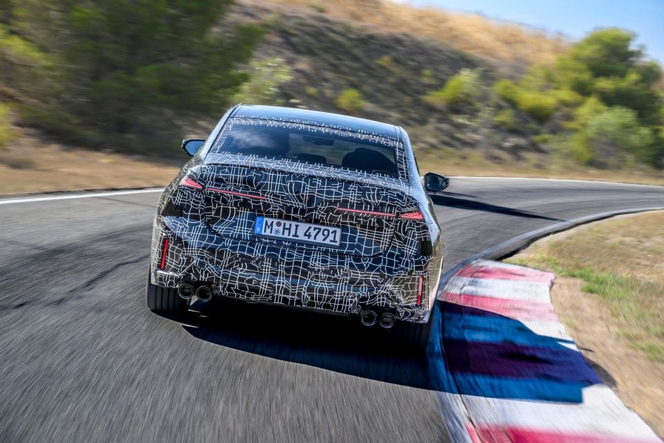 A camouflaged BMW 3 Series prototype seen from the rear, driving on a race track