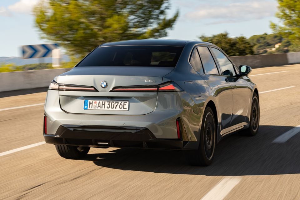 A grey 2027 BMW i350 sedan driving on a highway, seen from the rear quarter