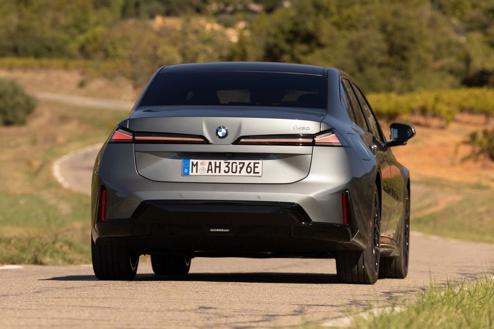 A grey BMW electric sedan driving along a winding country road, seen from the rear