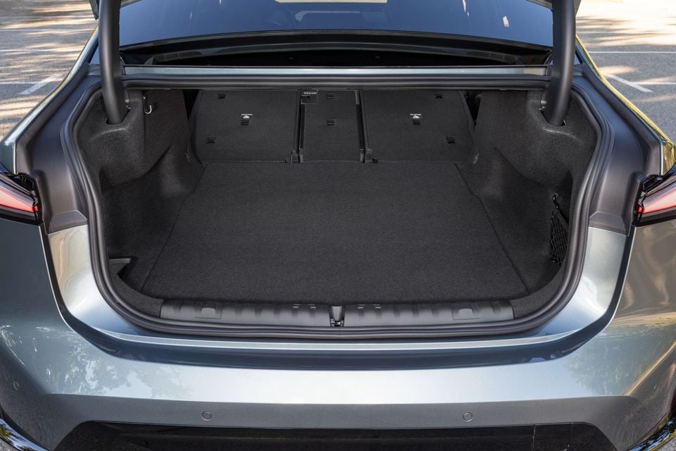 Open boot of a silver-grey 2027 BMW i3 50 sedan, showing the carpeted cargo floor and folding rear seatbacks