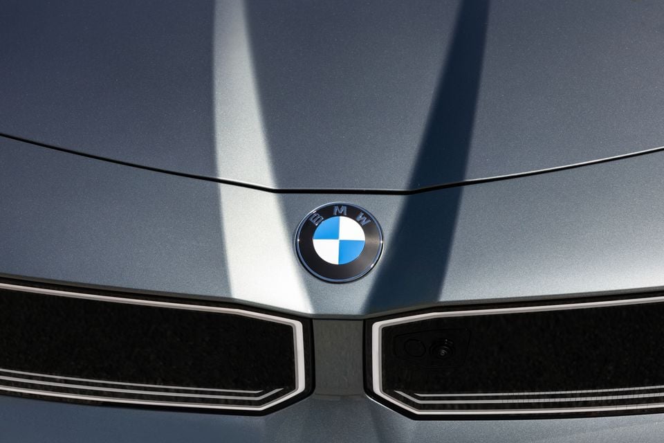 Close-up of the BMW roundel badge on the grey bonnet of a 2027 BMW i3 50, above its illuminated kidney grille outlines