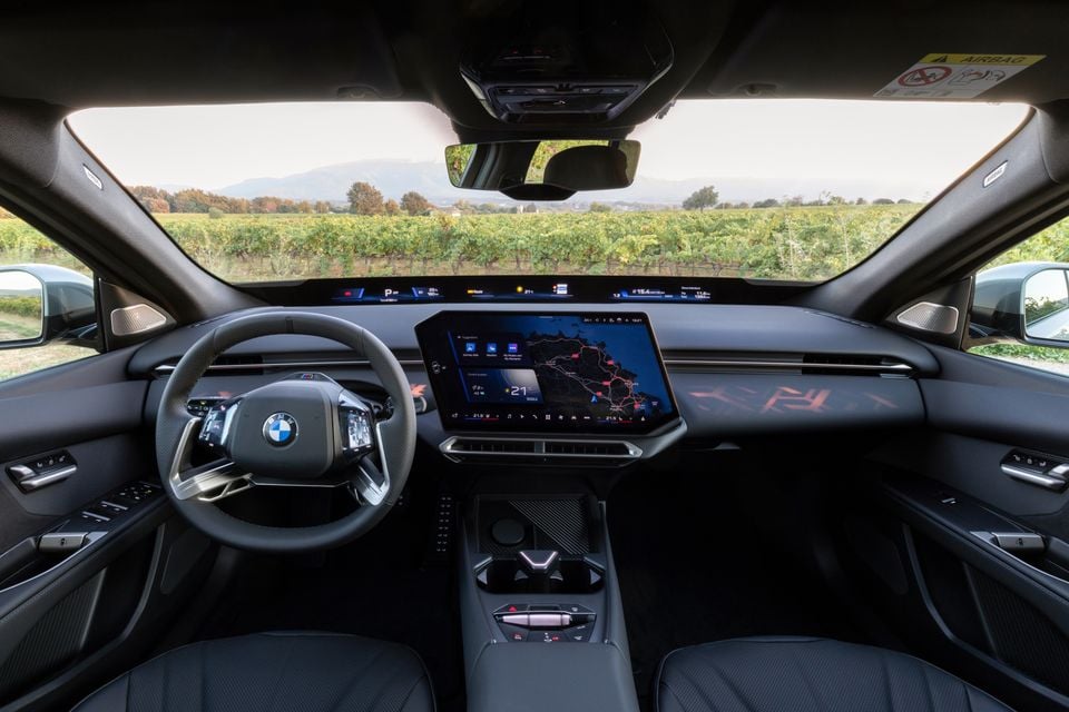 Dashboard of the 2027 BMW i3 50 showing the steering wheel, central touchscreen with navigation map and panoramic display, overlooking vineyards
