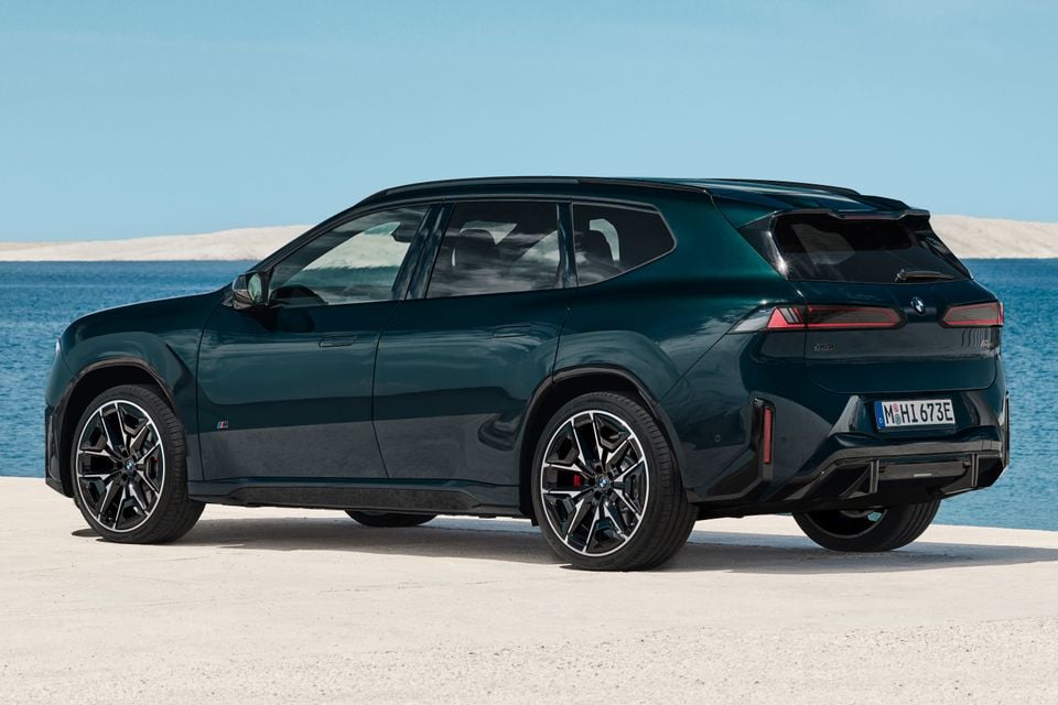 A dark green 2027 BMW iX3 M60 xDrive SUV parked by the sea, seen from the rear left side