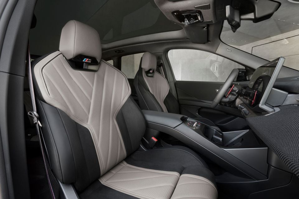 Front seats of the 2027 BMW iX3 M60 xDrive with grey and black leather M sport seats, centre console and steering wheel, seen from the passenger door