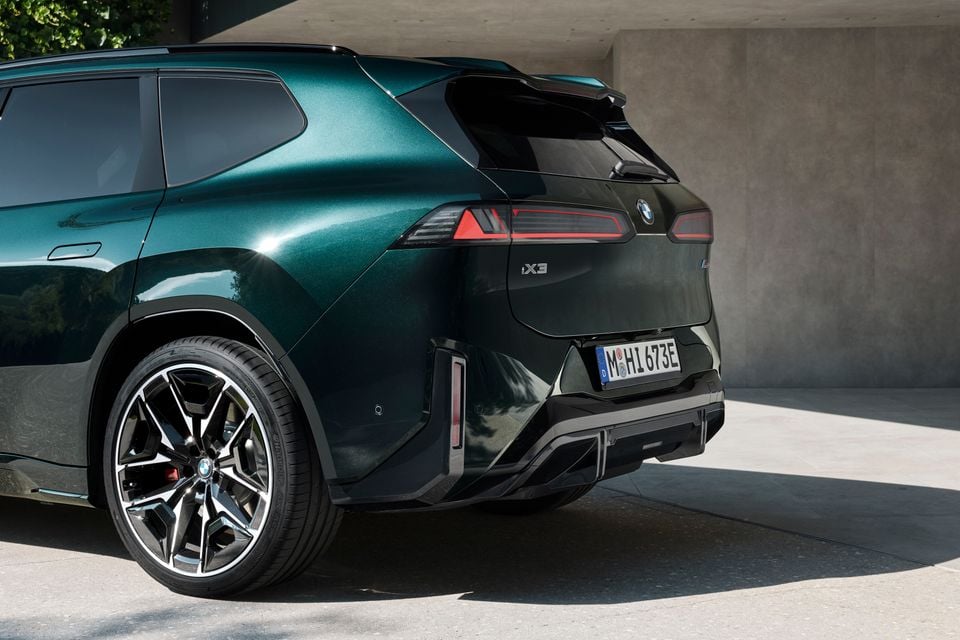 Rear quarter of a dark green 2027 BMW iX3 M60 xDrive electric SUV, showing its tail-lights, rear bumper and large alloy wheel