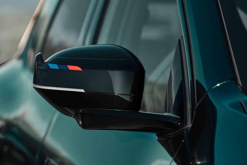 Close-up of the gloss black side mirror with M-colour stripes on a green 2027 BMW iX3 M60 xDrive