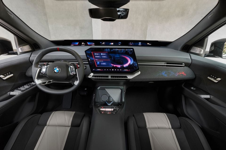 Dashboard of the 2027 BMW iX3 M60 xDrive with a flat-bottom steering wheel, panoramic display across the windscreen base, central touchscreen and front seats