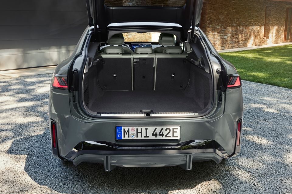 The open boot of a grey 2027 BMW iX4 shows a large cargo area with the rear seats folded flat.