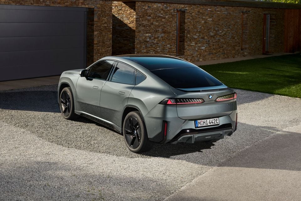 A grey 2027 BMW iX4 electric SUV coupe parked in a driveway, seen from the rear quarter
