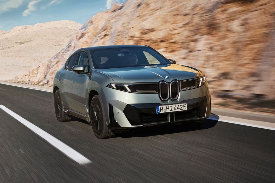 A silver BMW iX4 SUV driving on a mountain road, seen from the front quarter view.