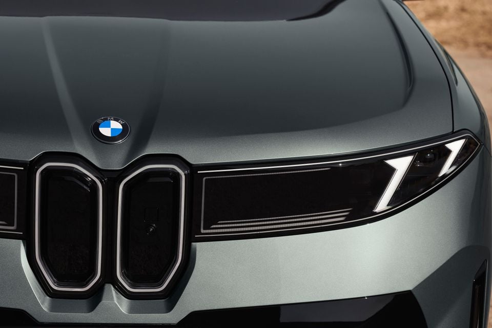 Close-up of a grey BMW iX4's front end, showing the kidney grille, headlight and bonnet with the BMW badge.