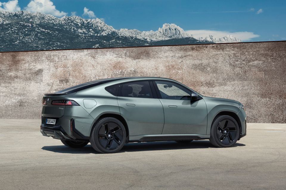 A grey 2027 BMW iX4 50 xDrive electric SUV coupe photographed from the side with mountains in the background.