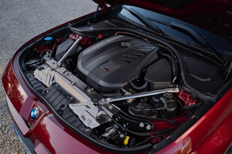 Engine bay of a red 2027 BMW M350 3 Series with the bonnet open, showing the M-badged engine cover and strut braces