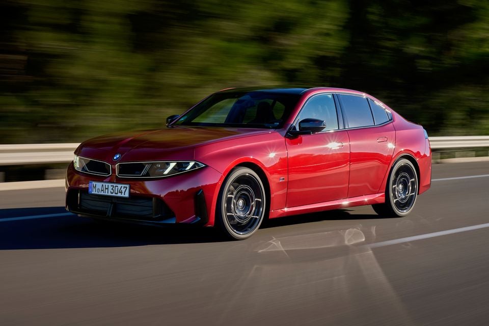 A red 2027 BMW M350 3 Series sedan driving on a highway, seen from the front left side