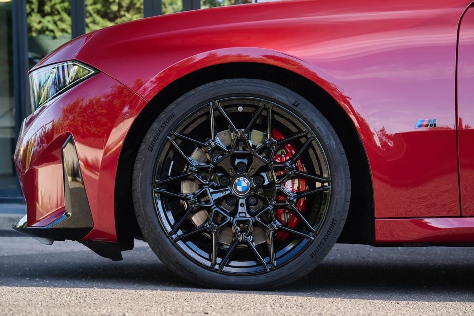 Close-up of the black alloy wheel, red brake caliper and M badge on the front guard of a red 2027 BMW M350 3 Series