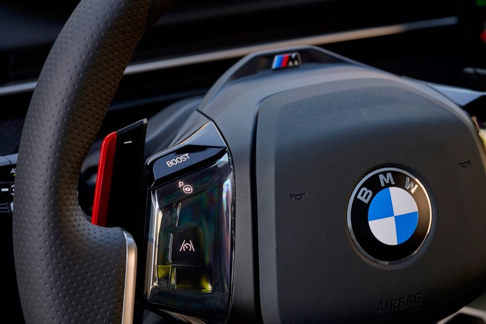 Close-up of the 2027 BMW M350 steering wheel showing the BMW roundel, M badge, illuminated Boost button and red shift paddle