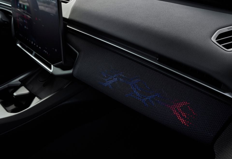 Close-up of the dashboard trim panel in a 2027 BMW M3 with an illuminated ambient light pattern glowing in blue and red.