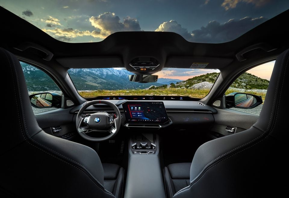 The interior of a BMW M350, showing the dashboard, steering wheel and curved display screens with mountains visible through the windscreen.