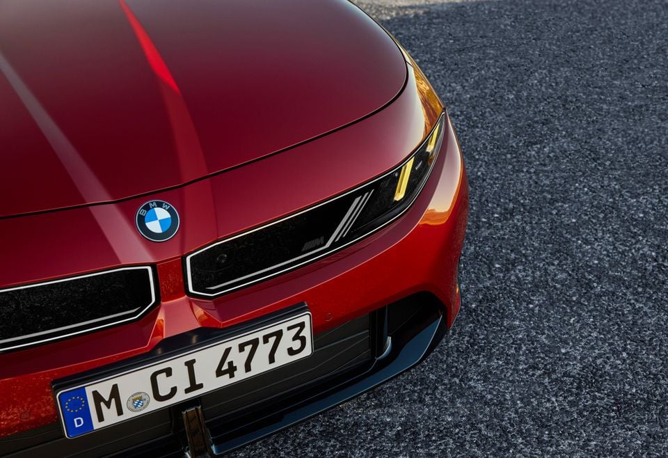 Close-up of the front end of a red 2027 BMW M350 xDrive, showing its headlight, grille and badge.